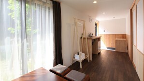 A room with a wooden bench, a wooden desk, a hanging clothes rack, and a view of greenery through sheer curtains. - B&B Neagari (Nomi)