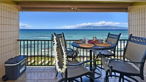 A balcony with a table and chairs, overlooking a beach and ocean. - SUMMER SALE! Oceanfront Condo w AC, Ocean Views & Heated Pool - Kaleialoha 309 (Lahaina)