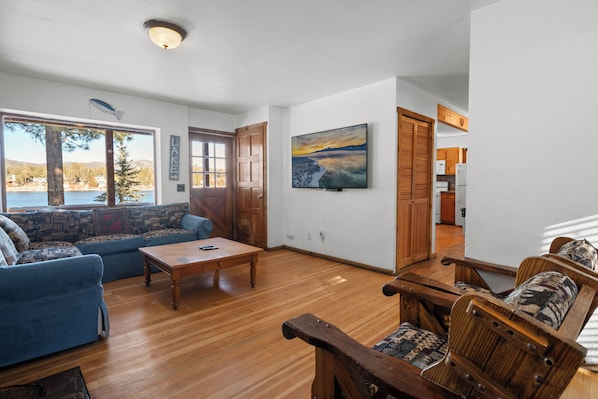 A spacious living room with a large window, a sofa, a wooden coffee table, and a painting on the wall.