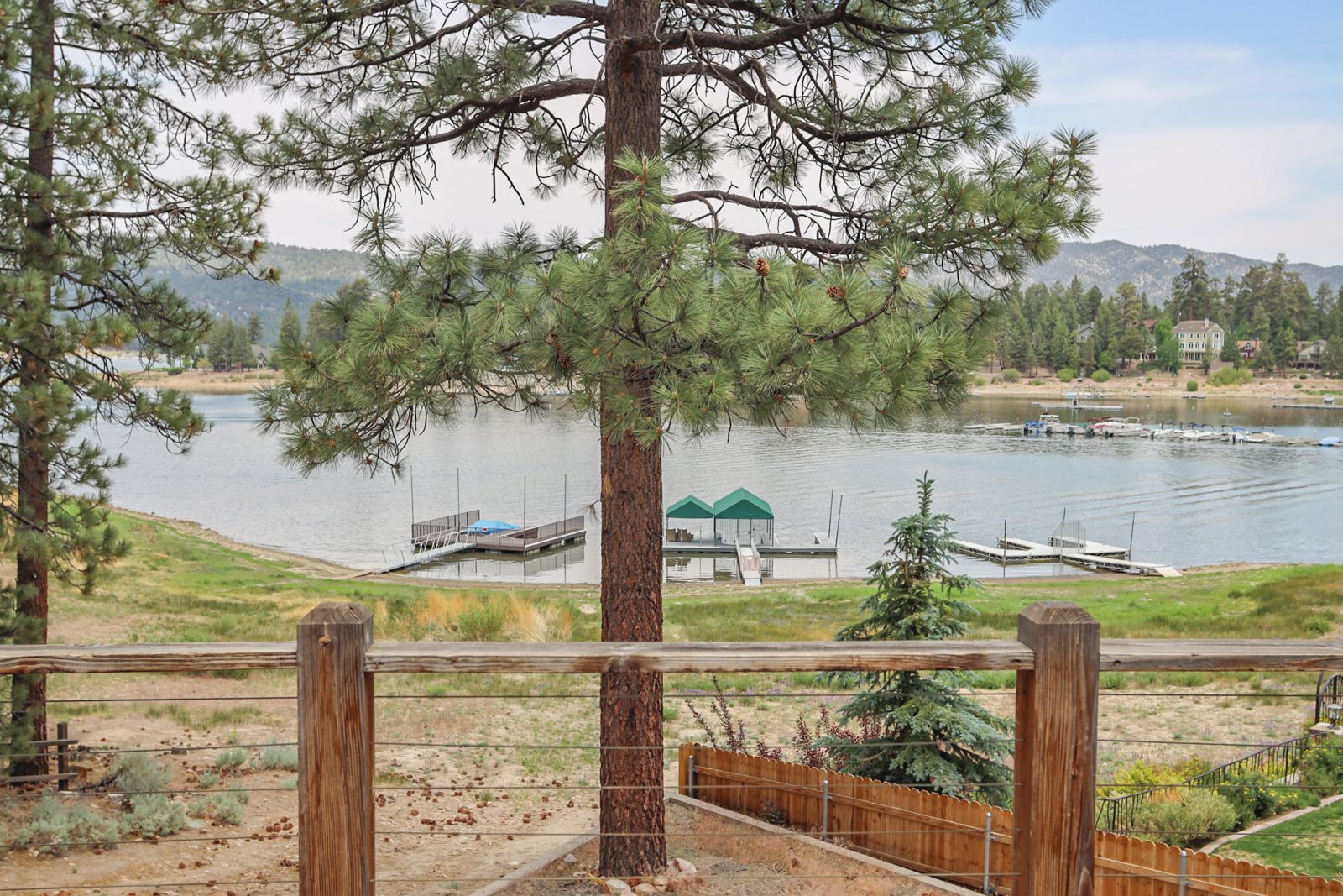 Vista de un lago con botes amarrados, una cerca de madera y un árbol en primer plano.