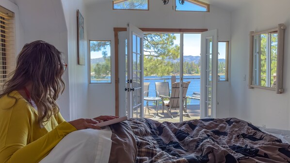 A bedroom with a bed, a window, and a view of a balcony with chairs and a table.