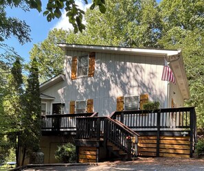 Une maison à deux étages avec un porche à l’avant, une terrasse en bois et un drapeau américain.