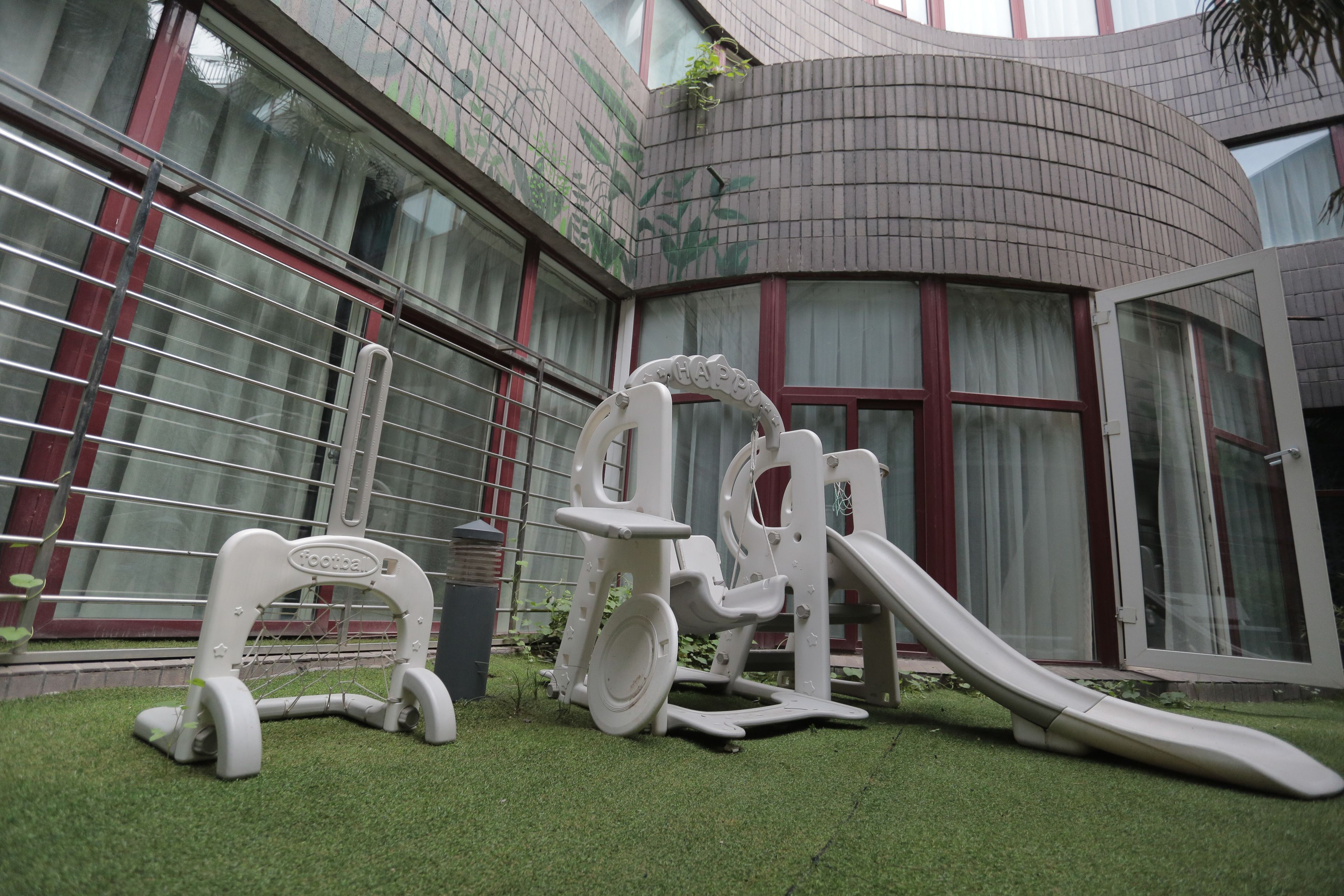 A playground with a slide and climbing structures in front of a building with large windows and a curved facade.