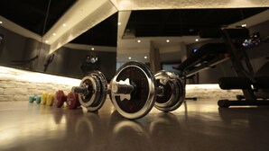 A row of dumbbells on a gym floor with a brick wall and ceiling lights.