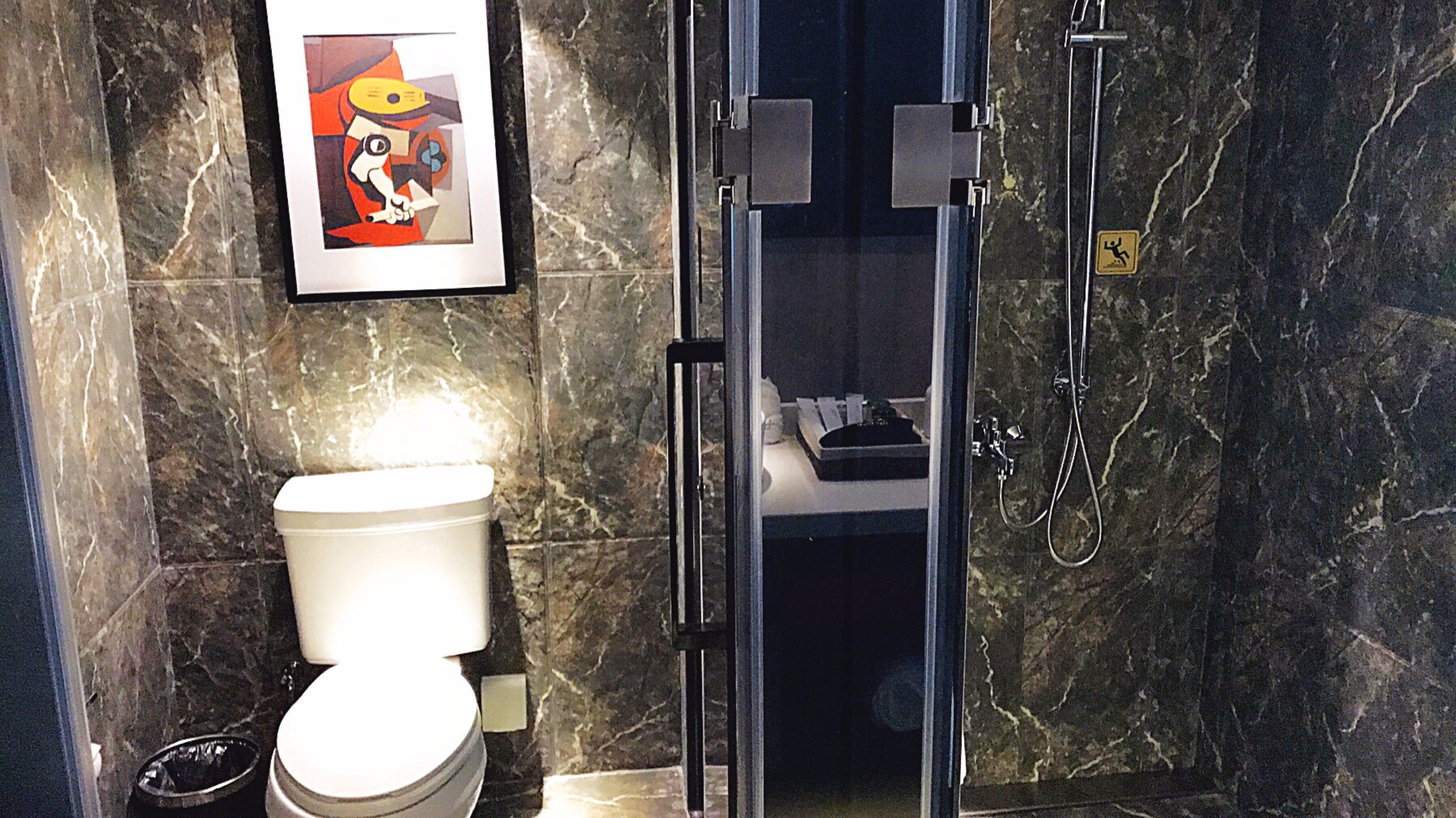 A bathroom with a toilet, a shower, and a marble wall.