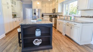 A kitchen with white cabinets, granite countertops, a black island, and a window providing natural light. - Beach comfort-lovely home, beach, pools, pet friendly! (Long Neck)