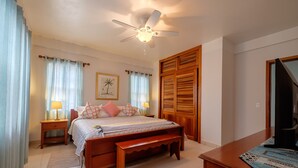 A bedroom with a bed, bedside tables, a ceiling fan, a wooden wardrobe, and a television. - Sunset Beach "B1" - Beachfront At Its Best Plus Pool, Kayaks, Bikes & More 🏖 (San Pedro Town)