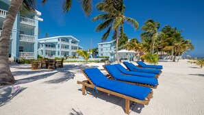 Ein Hotel direkt am Strand mit mehreren blauen Balkonen, LiegestĂŒhlen und Palmen.