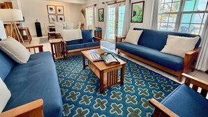 A living room with blue sofas, a coffee table, and a ceiling fan. - Sunset Beach "B1" - Beachfront At Its Best Plus Pool, Kayaks, Bikes & More 🏖 (San Pedro Town)