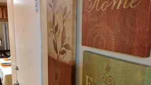Un corridoio con una porta bianca, una parete decorata con tre quadri e un'area pranzo sullo sfondo.