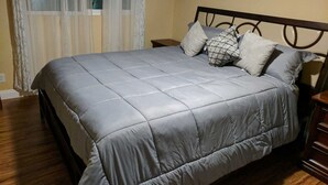 Camera da letto con un letto grande, una testiera in legno, un comodino, una sveglia e una finestra con tende.