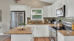 A modern kitchen with white cabinets, a granite countertop, stainless steel appliances, and a window with blinds.