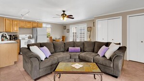 A living room with a sectional sofa, a coffee table, and a kitchen area with wooden cabinets and appliances. - Tucson Desert Rendezvous (Tucson)