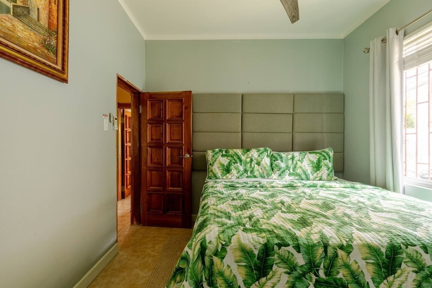 Un dormitorio con cama, puerta de madera y ventana con cortinas.