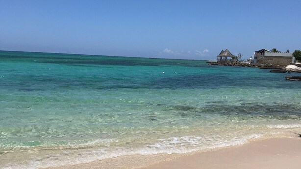A beach with clear turquoise water, a sandy shore, and a structure with a thatched roof.