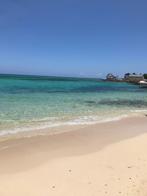 A beach with clear turquoise water, a sandy shore, and a structure with a thatched roof.