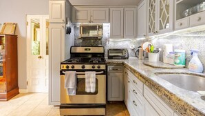 A kitchen with a stove, oven, microwave, and a sink. There are cabinets and a countertop with various items.