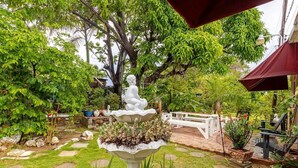 A garden with a white fountain, a white bench, and various plants.