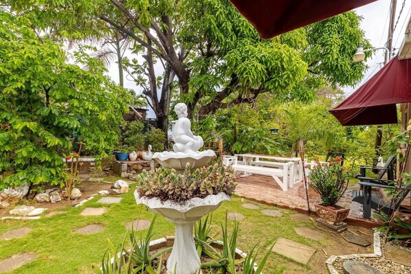 A garden with a white fountain, a white bench, and various plants.