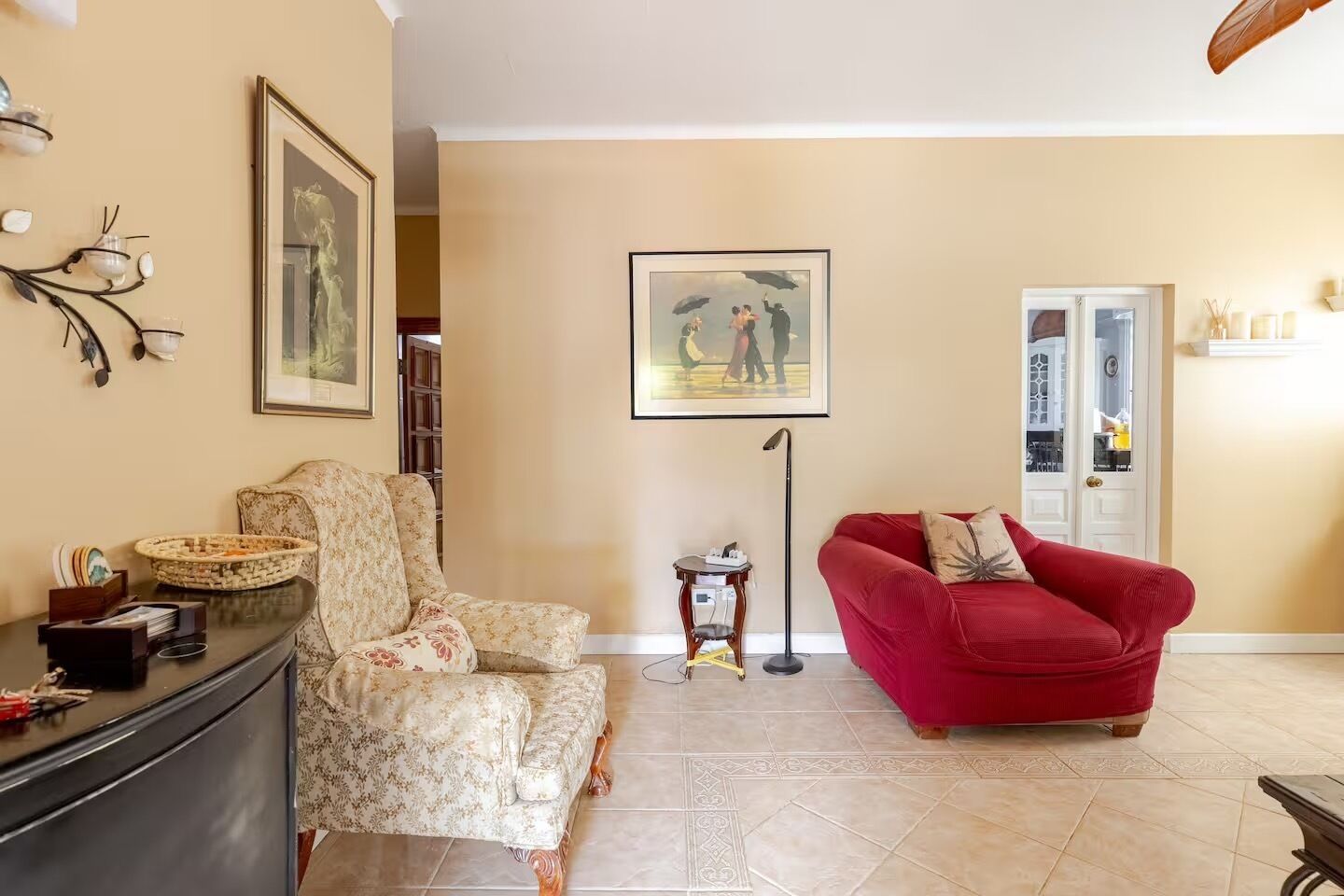 Ein Wohnzimmer mit einem blumengemusterten Sessel, einem roten Sofa, einer Stehlampe und einem gerahmten Gemälde an der Wand.