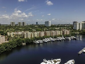 Boats docked in a tranquil marina surrounded by lush greenery and multi-story buildings with balconies.