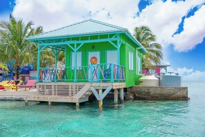 Een structure in turquoise en groen met een balkon, gelegen op een steiger boven helder turquoise water.