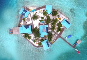 Vista aèria d'una illa turística tropical amb diverses piscines, palmeres i un moll amb un vaixell.