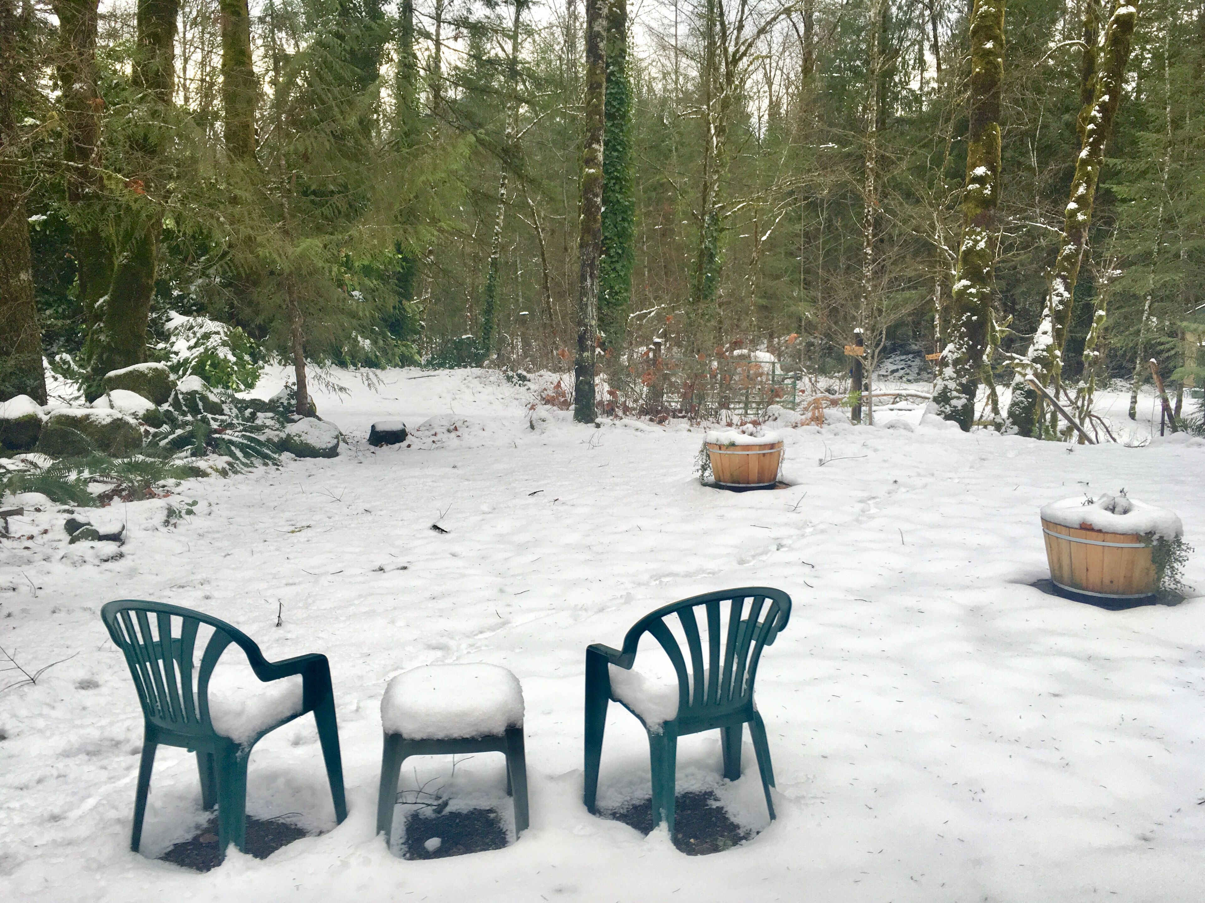 A snow-covered outdoor area with two green plastic chairs and a wooden bench.
