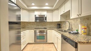 Una cocina con gabinetes blancos, electrodomésticos de acero inoxidable, encimera de granito y salpicadero de azulejos.