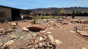 A landscaped garden with a wooden bridge, large rocks, and a view of mountains. - Beautiful Private Home W/ Large Living Spaces, Lots of Parking & Close to Trails (Moab)