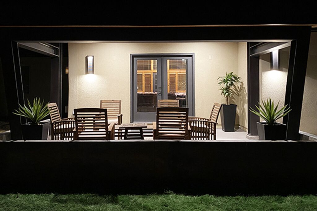 Un patio al aire libre con una mesa, sillas, plantas en macetas y una puerta con paneles de vidrio.
