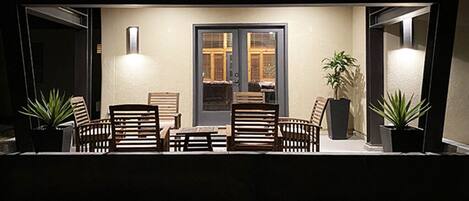 Un patio al aire libre con una mesa, sillas, plantas en macetas y una puerta con paneles de vidrio.