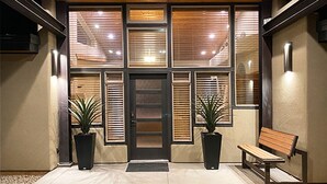 A building entrance with a wooden door, large windows with blinds, two potted plants, and a bench. - Beautiful Private Home W/ Large Living Spaces, Lots of Parking & Close to Trails (Moab)