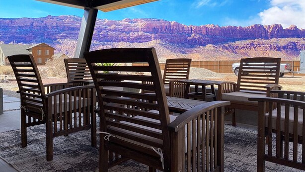 A covered outdoor seating area with wooden chairs and tables, overlooking a mountainous landscape. - Beautiful Private Home W/ Large Living Spaces, Lots of Parking & Close to Trails (Moab)