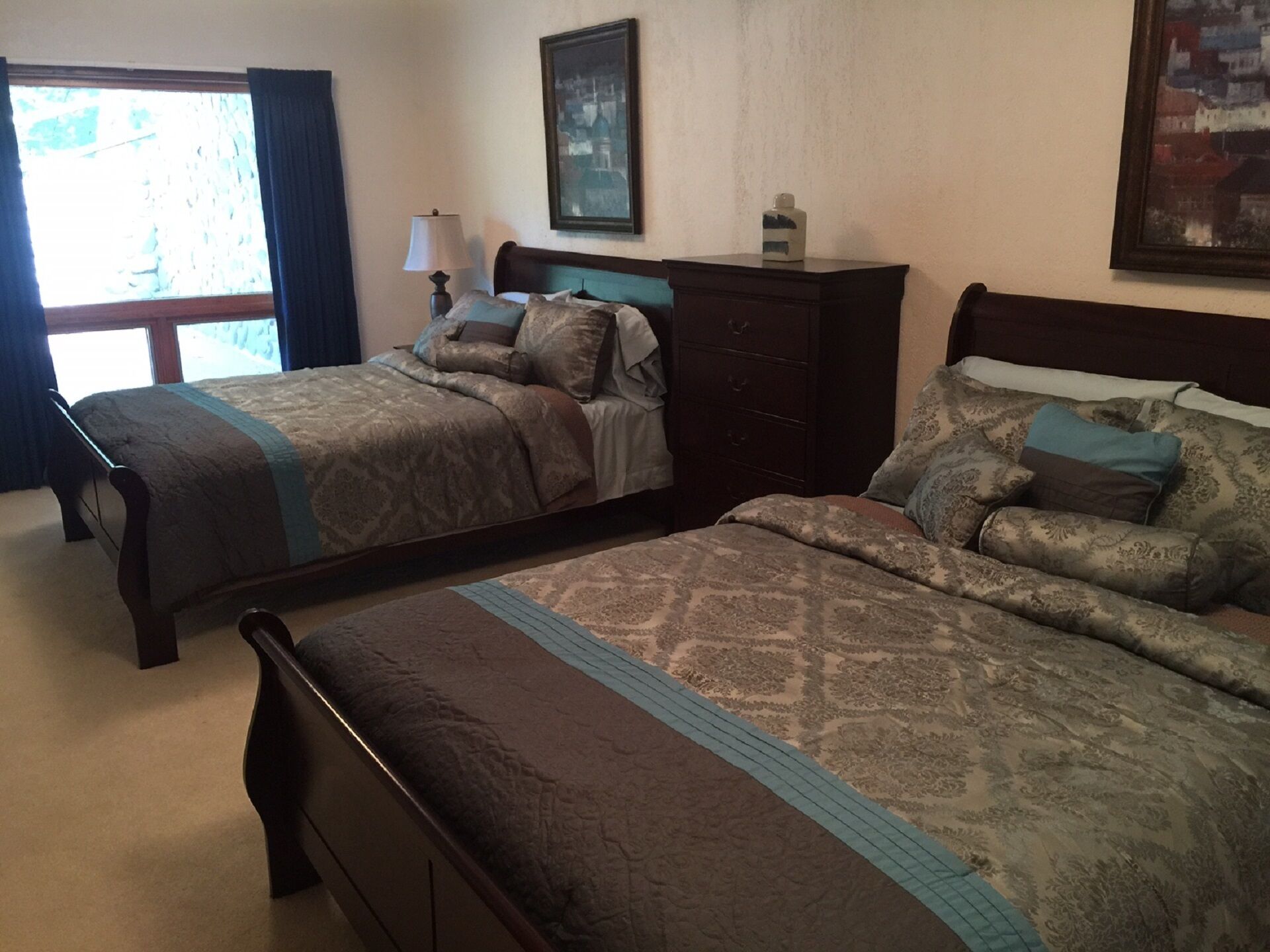 A bedroom with two beds, a dresser, a lamp, and a painting on the wall.