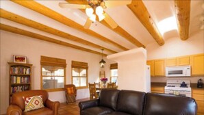 A cozy living room with a leather sofa and armchair, wooden beams on the ceiling, and a kitchen area with yellow cabinets and a microwave.