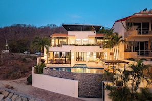 Une maison moderne à deux étages, dotée d’une piscine, de grandes fenêtres et d’une antenne parabolique.