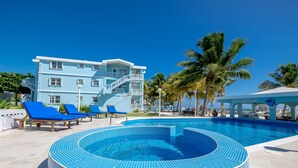 Une piscine aux bords recouverts de carreaux bleus, des chaises longues et un immeuble à plusieurs étages doté de balcons.