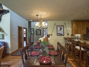 A dining room with a wooden table set for six, surrounded by wooden chairs. A chandelier hangs from the ceiling, and a vase with white flowers is on the table. - Beautiful Penthouse-Summer Heated Pool, Slopeside!, Fireplace, 3 king beds (Telluride)