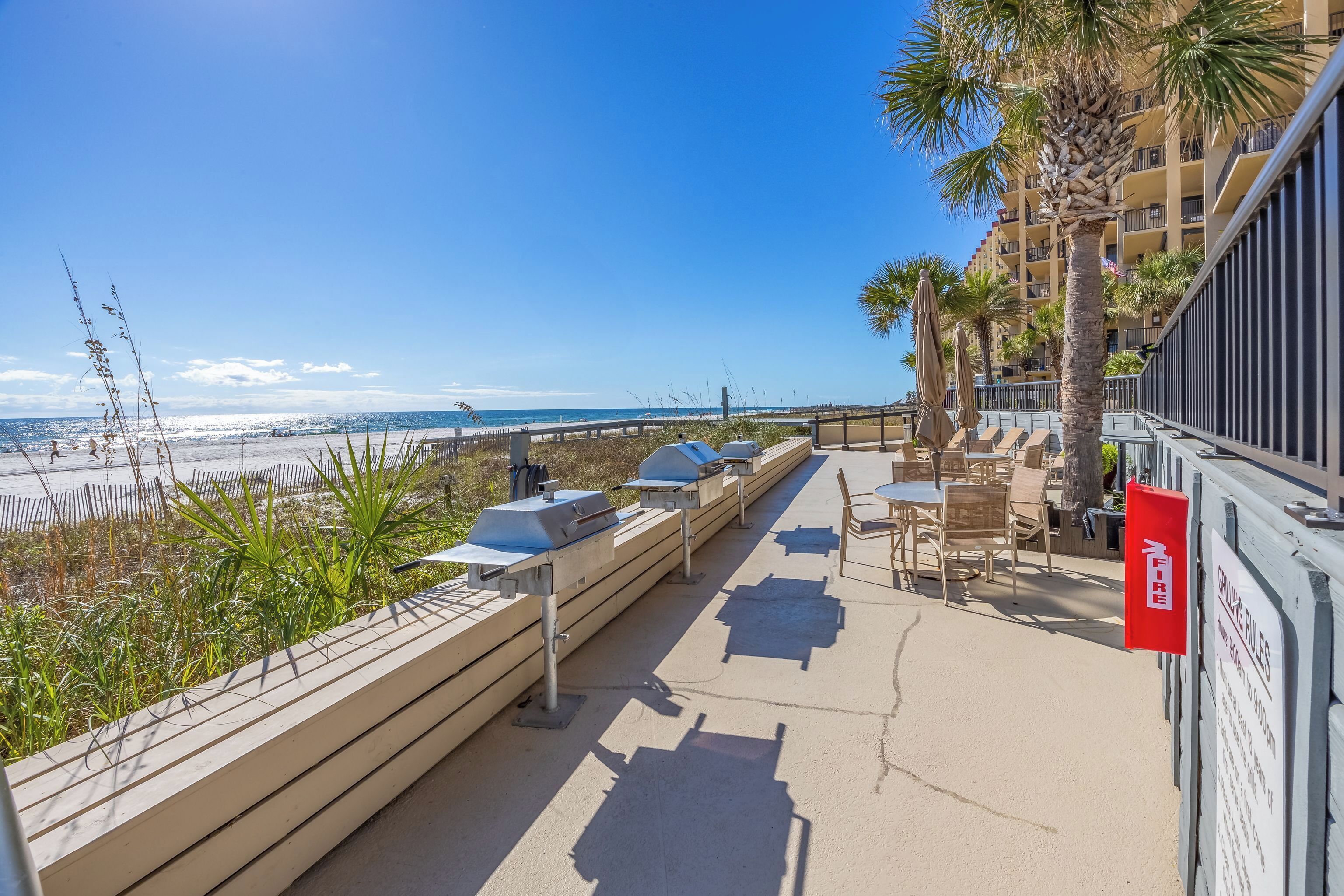 Une terrasse au bord de la plage, équipée de barbecues, de meubles pour s’asseoir à l’extérieur et offrant une vue sur l’océan.