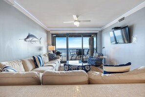 Sala de estar com sofá, ventilador de teto, TV e vista para o exterior.