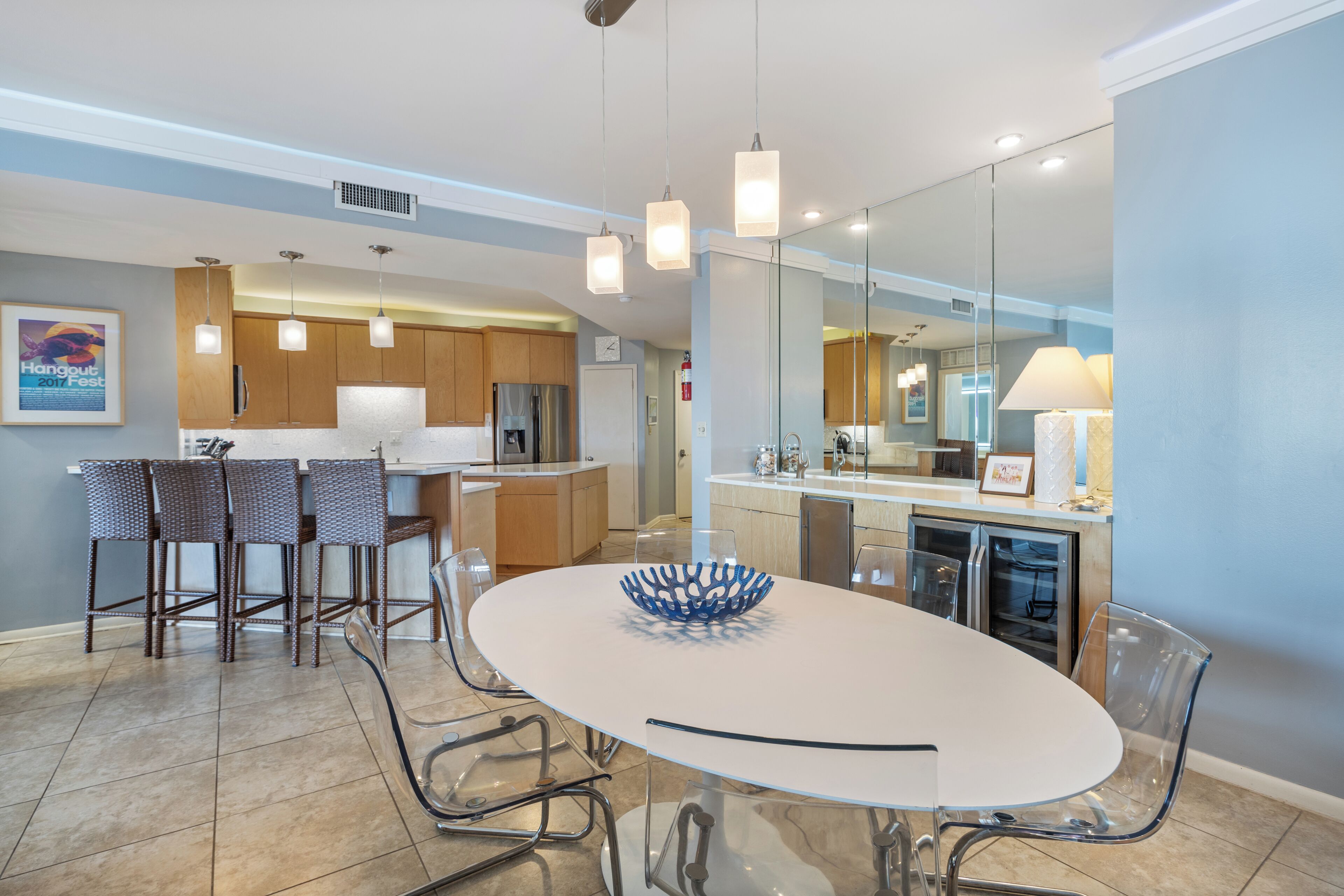 A modern kitchen with a dining area, featuring a white table, clear chairs, and pendant lighting.