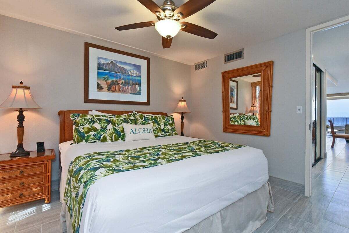 A hotel room with a bed, a ceiling fan, a framed picture on the wall, and a mirror.
