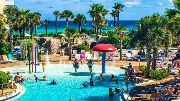 Un espace piscine comprenant plusieurs piscines, des palmiers et une plage en arrière-plan.
