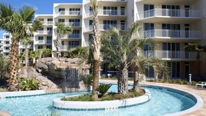 Un hôtel doté d’une piscine, de palmiers et d’une cascade décorative.