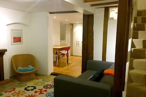 Una sala de estar con un sofá, una silla de mimbre, una mesa de comedor con sillas y una escalera.