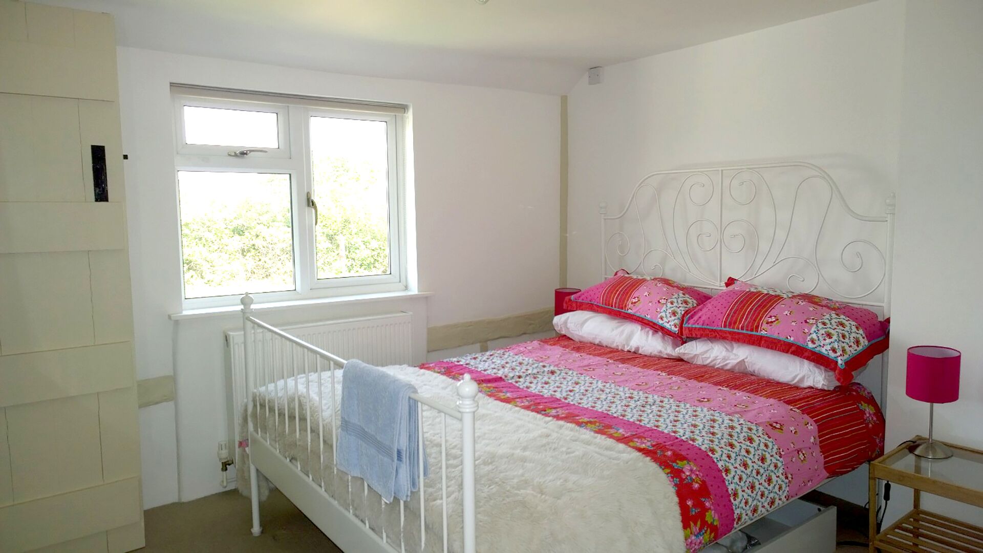 Een slaapkamer met een wit bed, een raam en een radiator.