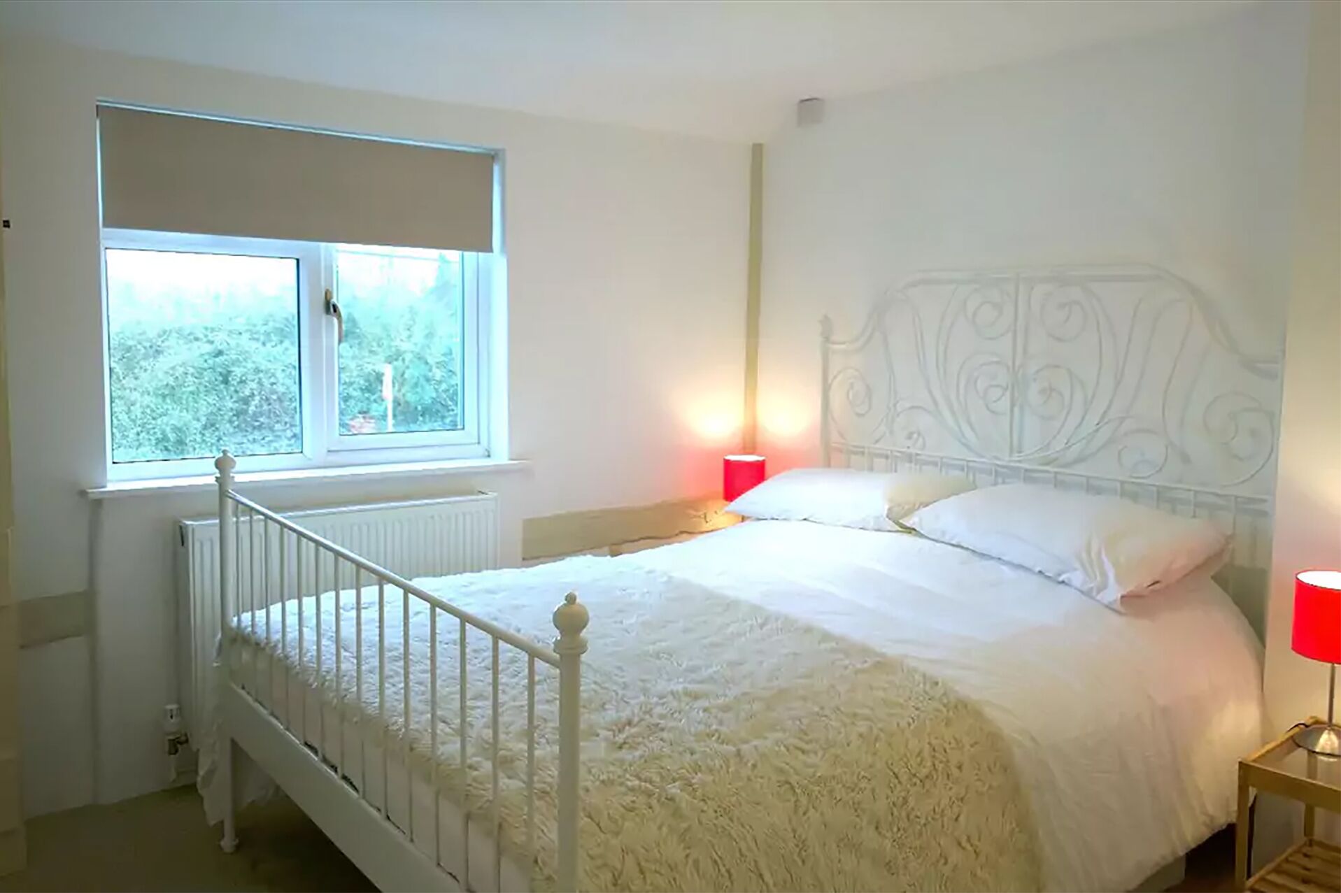 A bedroom with a white bed, a window with a view of trees, and a radiator.