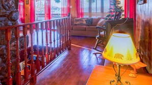 Ein gemütliches Blockhaus-Interieur mit Holzwänden, einem Steinofen, einer Holztreppe und einem Weihnachtsbaum.