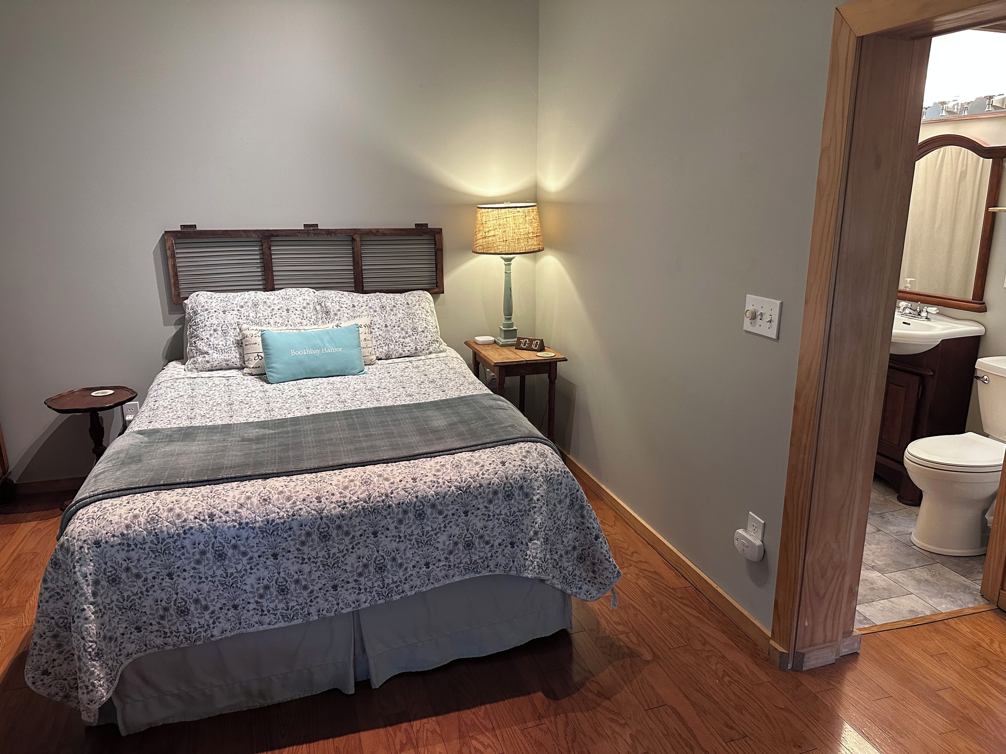 A bedroom with a bed, bedside table, lamp, and a view of the bathroom.